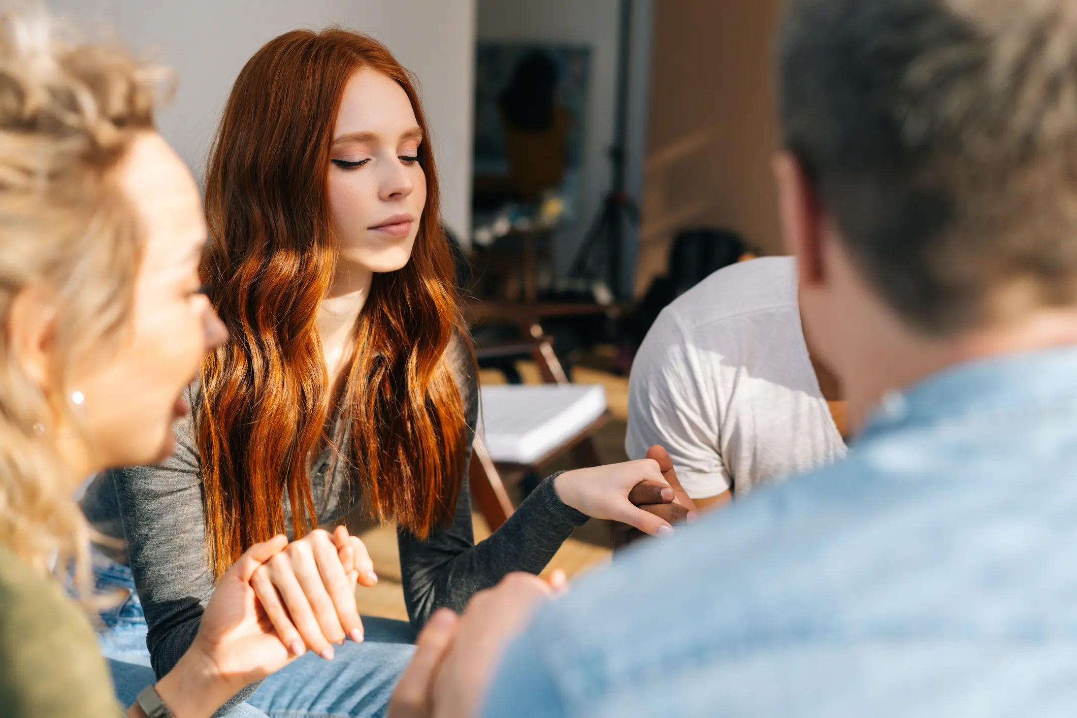 Group of young diverse multiethnic people holding hands together during the psychological therapy, meditating and solving together mental problems.